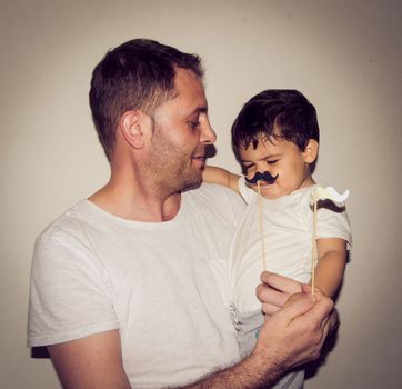 Father and son playng with moustache funny face expressions, family time