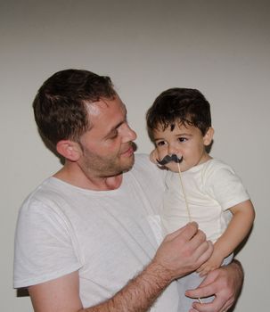 Father and son playng with moustache funny face expressions, family time