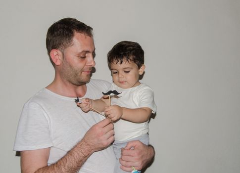 Father and son playng with moustache funny face expressions, family time