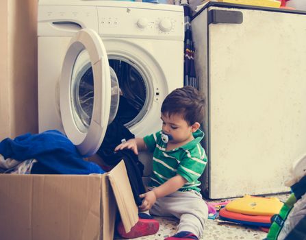 One and the half years old baby boy helping his mom by putting clothes in washing machine