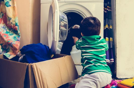 One and the half years old baby boy helping his mom by putting clothes in washing machine