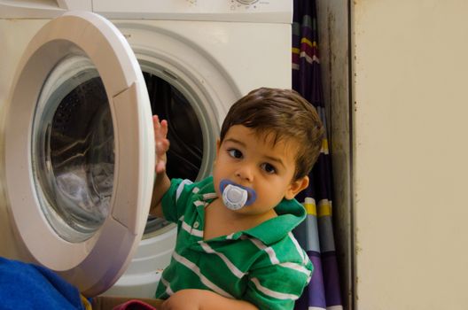 One and the half years old baby boy helping his mom by putting clothes in washing machine