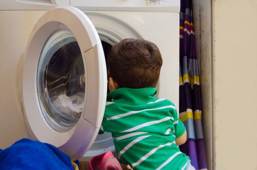 One and the half years old baby boy helping his mom by putting clothes in washing machine