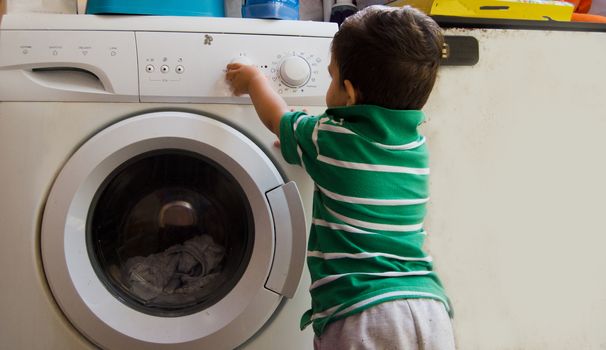 One and the half years old baby boy helping his mom by putting clothes in washing machine