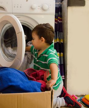 One and the half years old baby boy helping his mom by putting clothes in washing machine