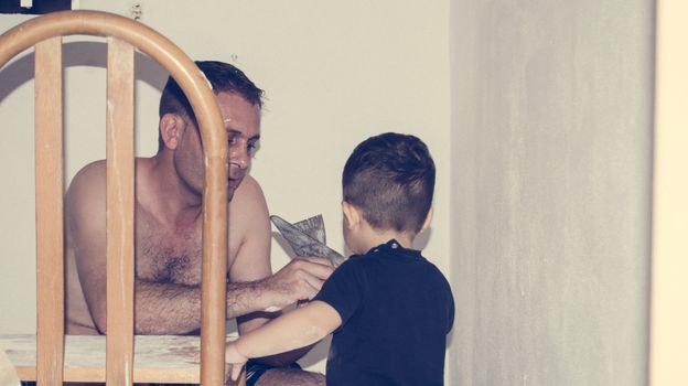 Father and one and half year old baby boy painting a room, little helper in the acction