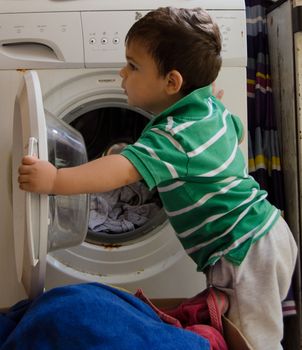 One and the half years old baby boy helping his mom by putting clothes in washing machine