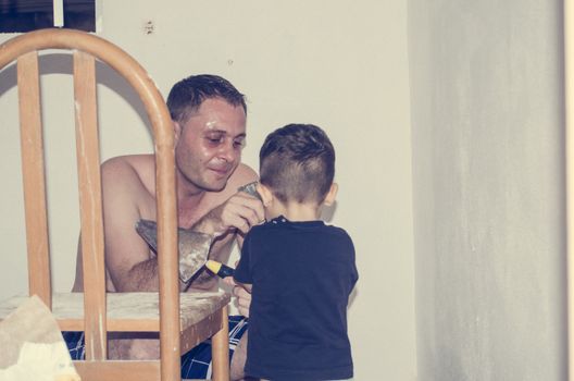 Father and one and half year old baby boy painting a room, little helper in the acction