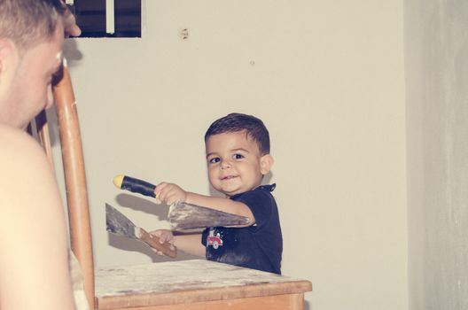 Father and one and half year old baby boy painting a room, little helper in the acction