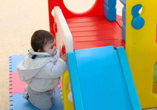 Baby boy playing with plastick house slide for toddlers