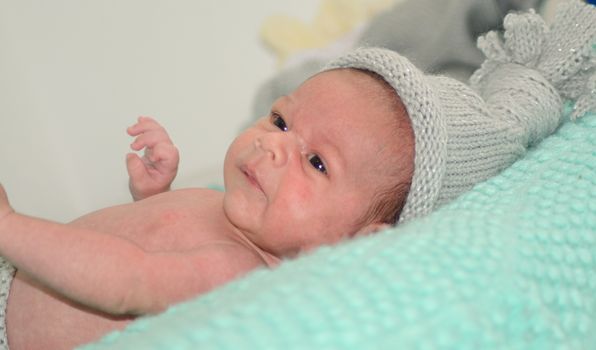 4 weeks old newborn baby boy with gray hat on green blanket