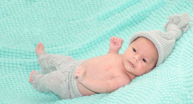 4 weeks old newborn baby boy with gray hat on green blanket