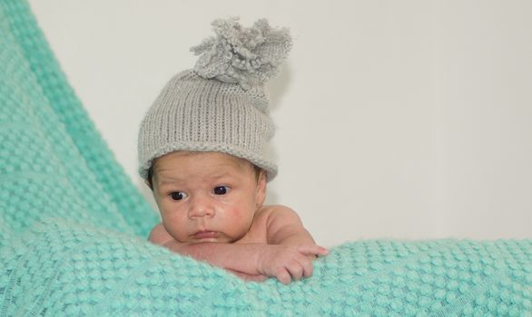 4 weeks old newborn baby boy with gray hat on green blanket copy space