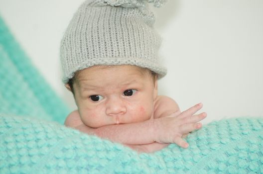 4 weeks old newborn baby boy with gray hat on green blanket
