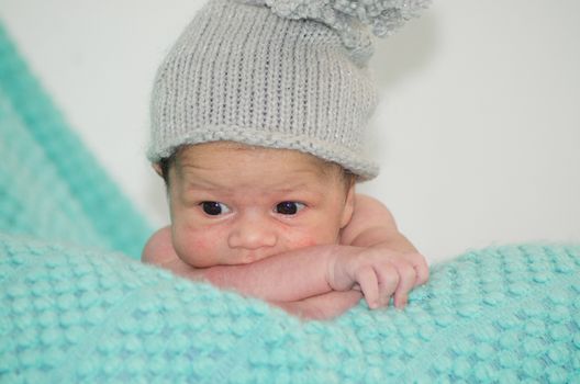 4 weeks old newborn baby boy with gray hat on green blanket