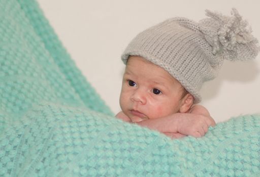 4 weeks old newborn baby boy with gray hat on green blanket