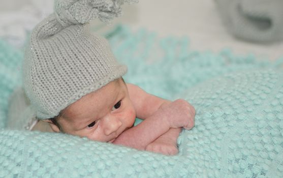 4 weeks old newborn baby boy with gray hat on green blanket copy space