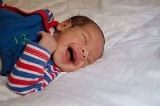 two weeks old newborn baby boy smilin while sleeping on white quilt, very cute smile