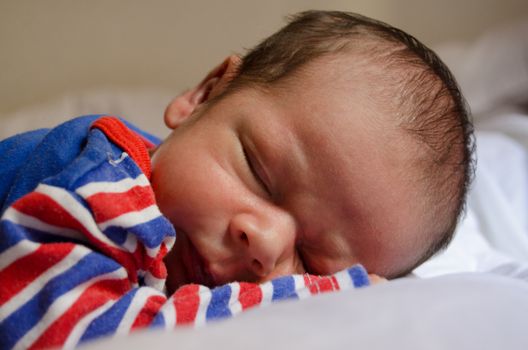 two weeks old newborn baby boy sleeping in blu red pijama on white quilt