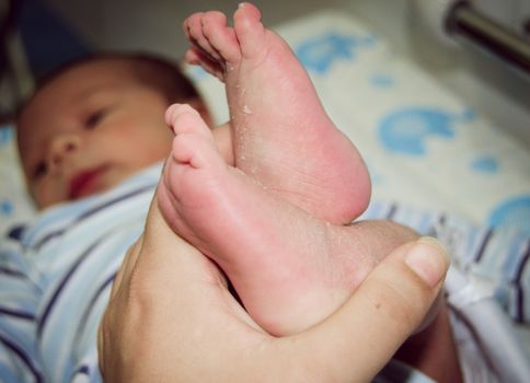 Mother massaging little newborn baby foot, close up