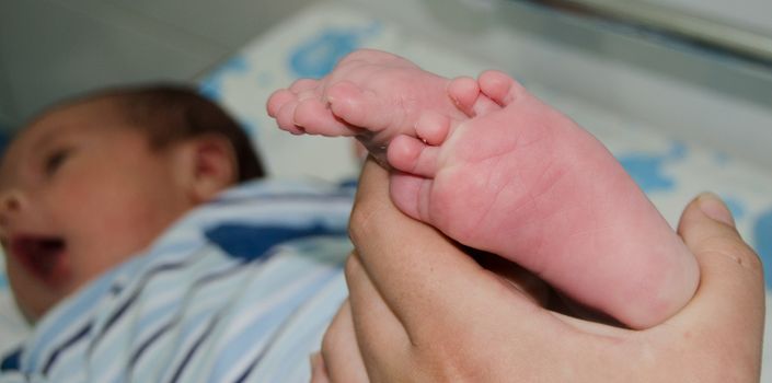 Mother massaging little newborn baby foot, close up