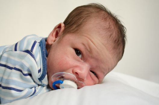 Newborn two weeks old baby boy laying down on white sheet awake, close up