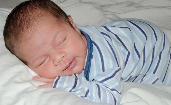 two weeks old newborn baby boy sleeping on white sheet, close up