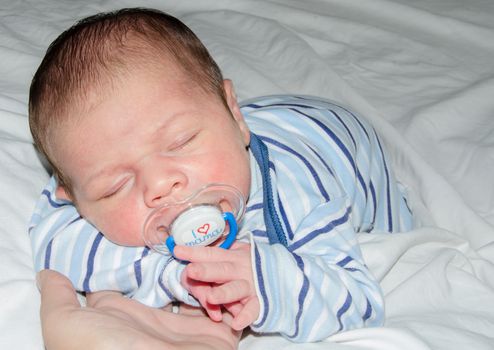 two weeks old newborn baby boy sleeping on white sheet, close up