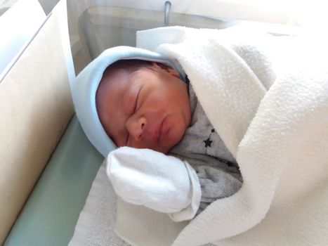 two days old newborn baby boy, sleeping in hospital cot, wraped in white blanket