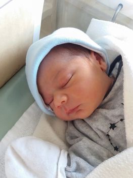 two days old newborn baby boy, sleeping in hospital cot, wraped in white blanket