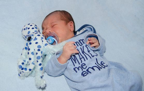 four days old newborn baby boy crying in the cot with octopus soft toy