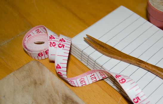 notebook with wooden fork and measuring tape on wooden table, diet and healty eating concept