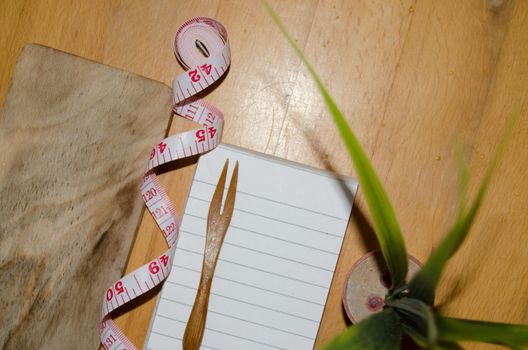 notebook with wooden fork and measuring tape on wooden table, diet and healty eating concept