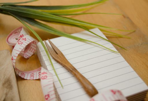 notebook with wooden fork and measuring tape on wooden table, diet and healty eating concept