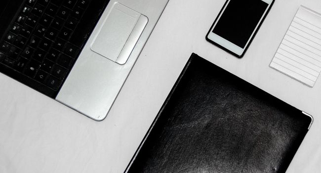 White office desk table with blank notebook, laptop and other office supplies. Top view with copy space, flat lay.