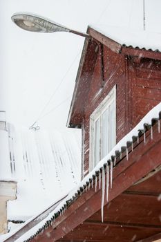 The roof of house covered with snow and icicles. Icicles hanging from roof. Winter in Latvia. Icicles hang from brown house roof. 