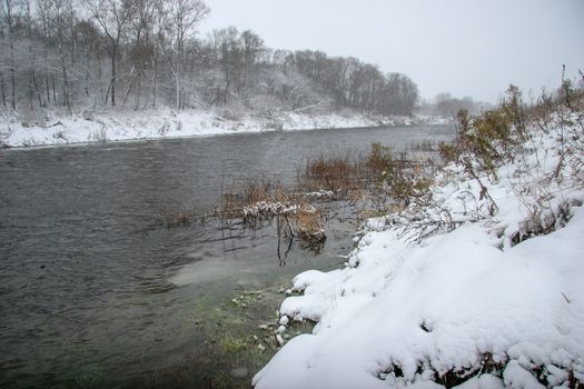 River landscape in winter. River with snow-covered coasts. River Memele in snowfall time. Winter in Latvia. Snow covered landscape with forest and riwer during the winter. 

