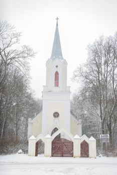 Church in snowfall. Winter in Barbele, Latvia. Church covered in snow. Winter landscape with snow covered church and trees.



