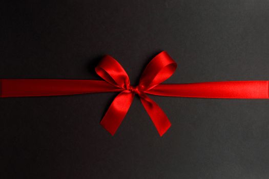 Shiny red satin ribbon and bow on black background. Holiday gift concept