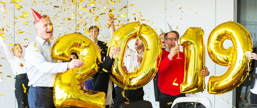 Business people celebrating 2019 New Year at office party holding golden balloons