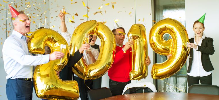 Business people celebrating 2019 New Year at office party holding golden balloons