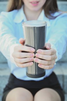 Girl student sitting on the steps during a working break, and offers to drink hot tea, close-up