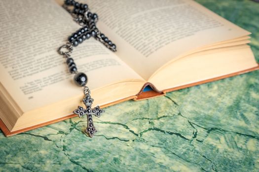 Black rosary and cross on the Bible on a green surface. Religion at school.