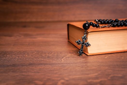 Black rosary and cross on the Bible at wooden table. Religion at school.vintage style.