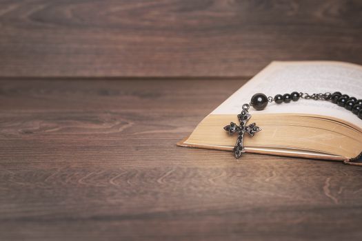 Black rosary and cross on the Bible at wooden table. Religion at school.vintage style.