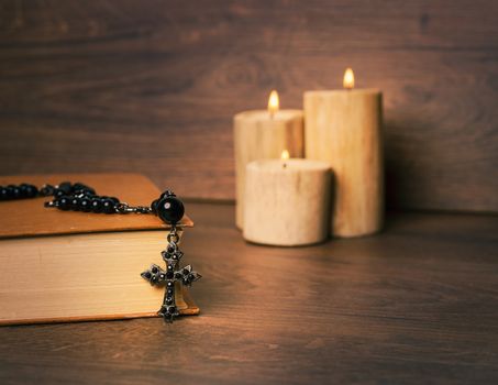 Black rosary and cross on the Bible at wooden table,background candle. Religion at school.vintage style.
