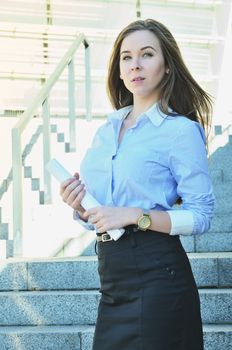 Beautiful young business woman standing near high architecture, outside and looking into the distance, vertical photo