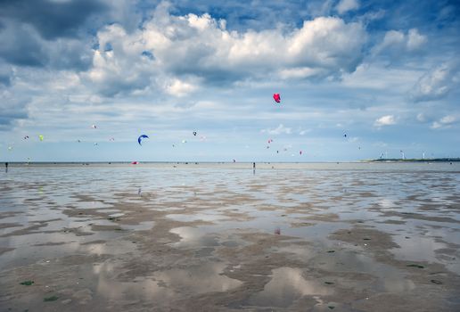 people sporting and kite surfing on the beach with clouds in the sky on a beach in holland