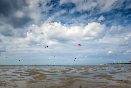 people sporting and kite surfing on the beach with clouds in the sky on a beach in holland