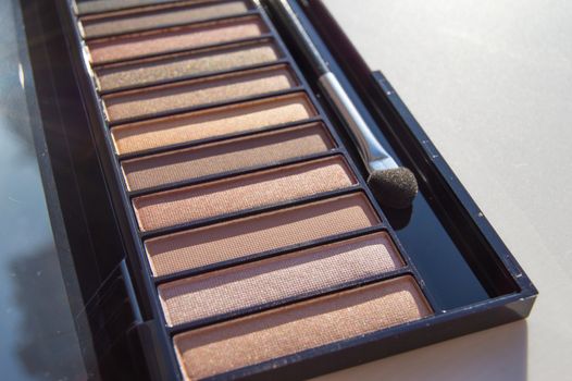Eye shadow in a palette of brown and Nude shades with a makeup brush.